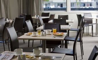 a well - arranged dining room with various tables and chairs arranged for a meal , including plates , cups , bowls , and utensils at Ibis Styles Canberra Tall Trees
