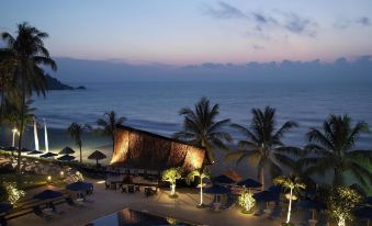 a beachside resort with a pool surrounded by palm trees , chairs , and umbrellas at night at Hyatt Regency Kuantan Resort