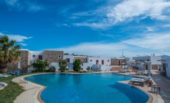 a beautiful swimming pool area with white buildings , blue sky , and clear water , surrounded by lush greenery at Naxos Palace Hotel