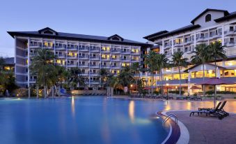 a large resort with multiple buildings , a swimming pool , and palm trees at dusk , under the glow of lights at Thistle Port Dickson Resort
