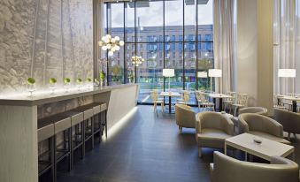 a modern hotel lobby with a bar , seating area , and large windows overlooking the city at NH Parma