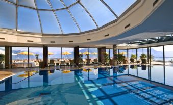 a large indoor swimming pool with a skylight , surrounded by lounge chairs and umbrellas , and overlooking the ocean at Le Mirador Resort and Spa