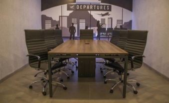 a conference room with a wooden table surrounded by black chairs , and a large mural on the wall at Hangar Inn Guadalajara Aeropuerto