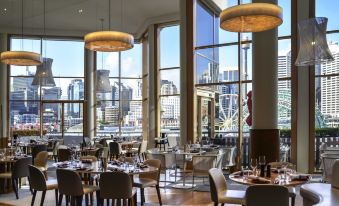 a modern restaurant with large windows overlooking the city , featuring tables and chairs set for dining at Novotel Sydney Darling Harbour