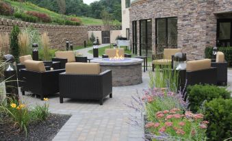 a patio area with several chairs and a fire pit surrounded by plants and flowers at Courtyard Oneonta Cooperstown Area