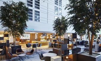 a modern restaurant with outdoor seating and a large tree in front of it , creating an inviting atmosphere at London Heathrow Marriott Hotel