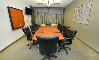 a conference room with a long table , black chairs , and an orange tablecloth , set against a backdrop of large windows and a television at SpringHill Suites Grand Forks