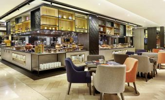 a modern restaurant with a dining area featuring colorful chairs and a variety of food on display at Novotel Jakarta Mangga Dua Square