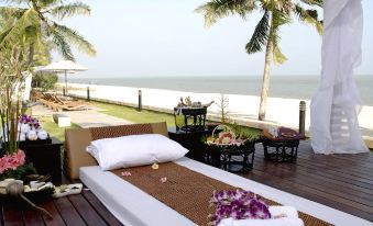 a bed with white linens and flowers on it is placed on a wooden deck overlooking the ocean at Kuiburi Hotel & Resort