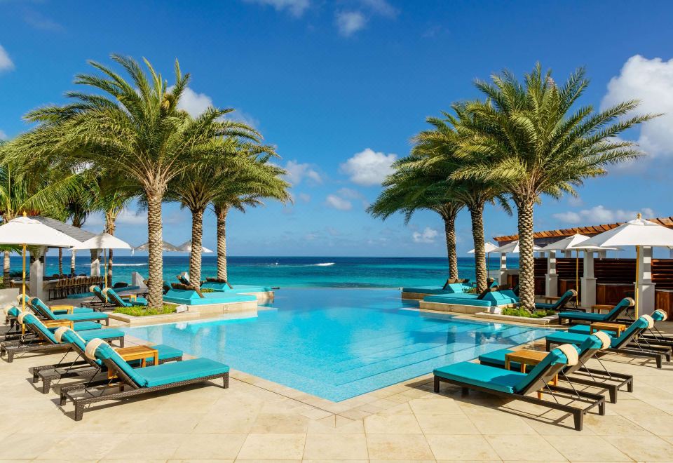 a large swimming pool surrounded by palm trees , with several lounge chairs and umbrellas placed around the pool at Zemi Beach House, LXR Hotels & Resorts