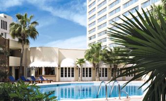 a hotel with a large pool surrounded by palm trees , chairs , and lounge chairs , as well as a building in the background at Amman Marriott Hotel