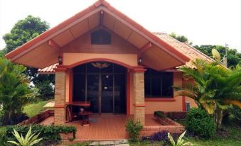 a small house with a red roof and brick pillars is surrounded by greenery and has a door at Baan Rim Khong Resort