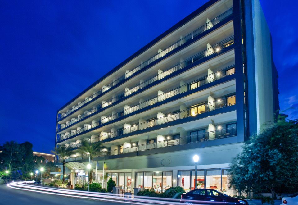 a modern building with a large parking garage and multiple levels , illuminated by lights against the dark blue sky at Mediterranean Hotel