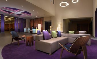 a modern lounge area with purple carpet , gray couches , and wooden tables , all lit by overhead lights at Hilton Garden Inn Monterrey Airport