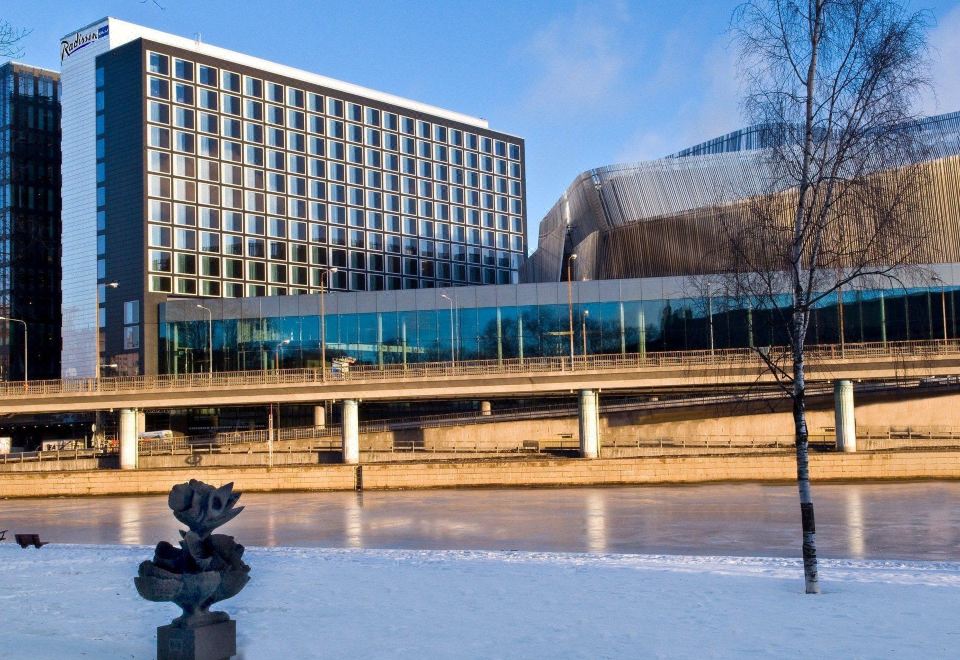 a large building is situated next to a frozen river with snow - covered trees and a small statue at Radisson Blu Waterfront Hotel, Stockholm
