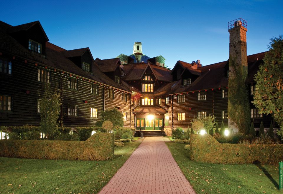 a large wooden mansion with a brick pathway leading up to the entrance , surrounded by greenery at Fairmont le Chateau Montebello
