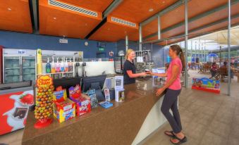 a woman is standing at a counter with various snacks and drinks in front of her at Ingenia Holidays Lake Conjola