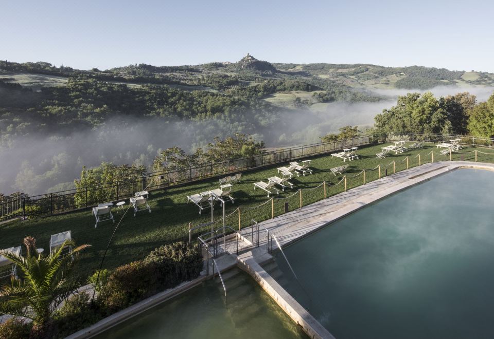 a serene landscape with a pool , trees , and mountains , set against a hazy sky , under the weather condition of a cloudy sky at Albergo Posta Marcucci
