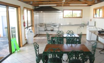 a spacious kitchen with white tiles , wooden floors , and green metal chairs around a wooden table at Robetown Motor Inn & Apartments