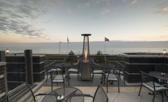 a rooftop patio with a fire pit and dining area overlooking the ocean at sunset at Cbh Hythe Imperial Hotel Golf and Spa