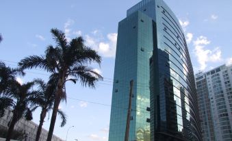 a tall glass building is next to a palm tree and a city street with other buildings at Hplus Vision Executive