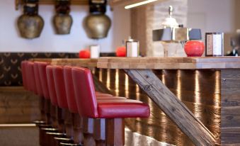 a modern bar with red leather chairs , wooden tables , and gold accents , creating an elegant atmosphere at Hotel Steinbock