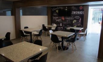 a modern cafeteria with black and white chairs and tables , a chalkboard wall , and an advertisement for strawberry lemonade at Hangar Inn Guadalajara Aeropuerto