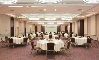 a large , well - lit banquet hall with multiple round tables set for a formal event , including white tablecloths , gold chairs , at Kichijoji Tokyu Rei Hotel