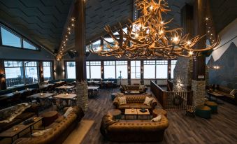 a large room with a wooden floor and ceiling , a chandelier hanging from the ceiling , and couches in the background at Mountain Lodge