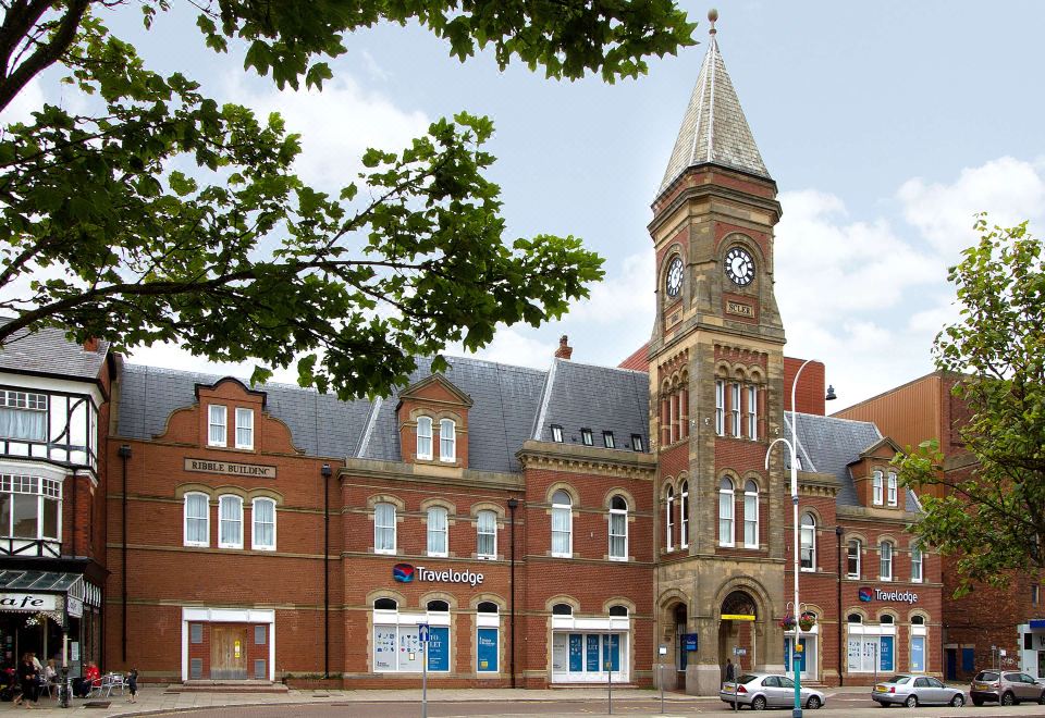 a brick building with a clock tower , surrounded by trees and other buildings in the background at Travelodge Southport