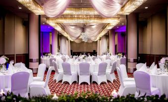 a large banquet hall with white chairs and tables , draped in white fabric , is adorned with chandeliers and flowers at Radisson Blu Hotel, Szczecin