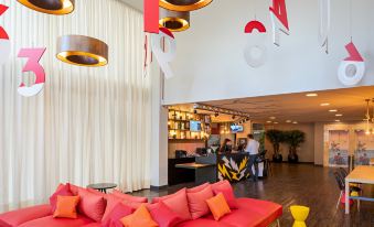 a modern lounge area with a red couch , multiple chairs , and hanging lights in a white - walled room at Ibis Styles Piracicaba