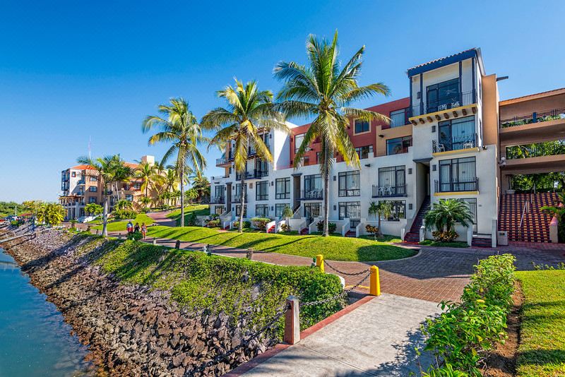 a row of beachfront condos with palm trees and grass , along with a path leading to the ocean at El Cid Marina Beach Hotel