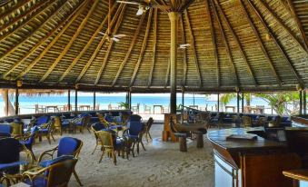 a restaurant with a thatched roof is situated on the beach , where people are sitting at tables and chairs at Makunudu Island