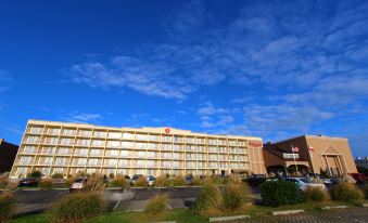 a large hotel with many cars parked in front of it , under a clear blue sky at Ramada Plaza by Wyndham Nags Head Oceanfront