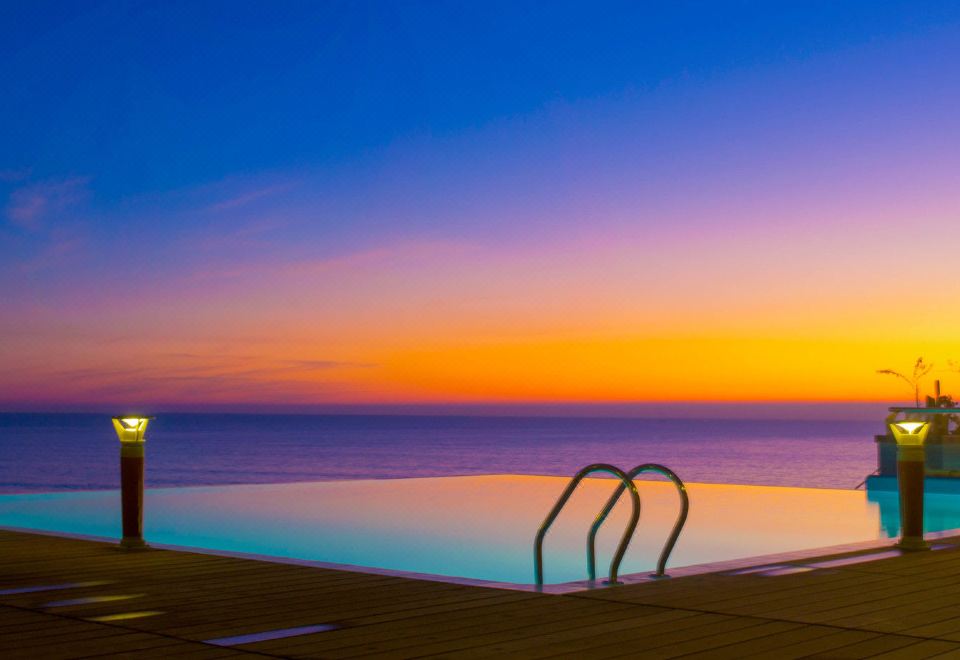 A swimming pool with a sunset view of water and mountains in the background during dusk at Sayeman Beach Resort