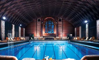 an indoor swimming pool with a wooden ceiling and walls , surrounded by lounge chairs and a dining area at Fairmont le Chateau Montebello