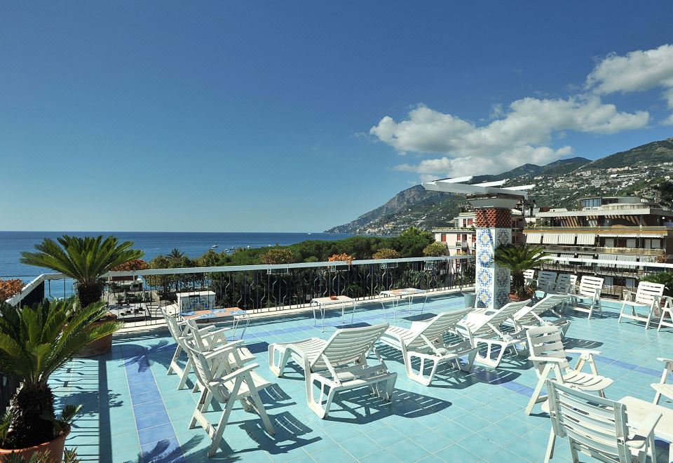 a large swimming pool with white lounge chairs and a mountainous view in the background at Hotel Miramare