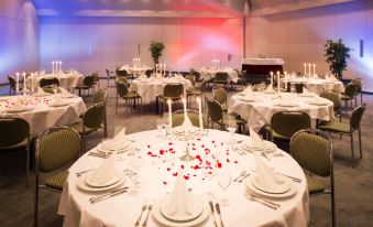 a large dining room with multiple tables covered in white tablecloths and adorned with red rose petals at Achat Hotel Kaiserhof Landshut