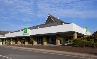 a large hotel building with a green sign on the front , situated in a parking lot at Holiday Inn Ipswich