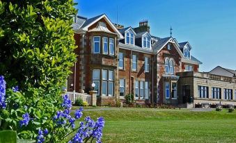 a large brick building with a green lawn in front of it , surrounded by trees at Seamill Hydro Hotel