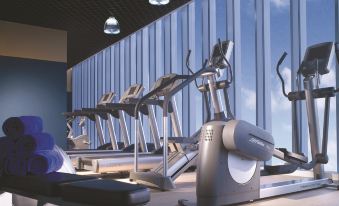 a gym with various exercise equipment , including treadmills and stationary bikes , under a large window at Oakwood Premier Cozmo Jakarta
