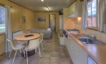 a kitchen with a sink , oven , and microwave is shown next to a dining area with a table and chairs at Kosciuszko Tourist Park