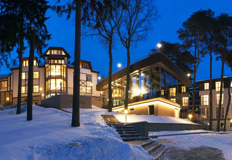 a snow - covered landscape with a large house surrounded by trees , lit up at night , and surrounded by snow at Hotel Universal