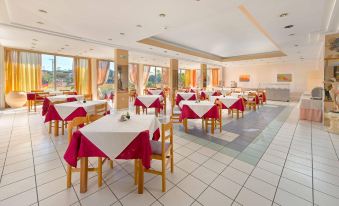 a large , well - lit restaurant with multiple dining tables and chairs , all set for a meal at Bayside Hotel Katsaras