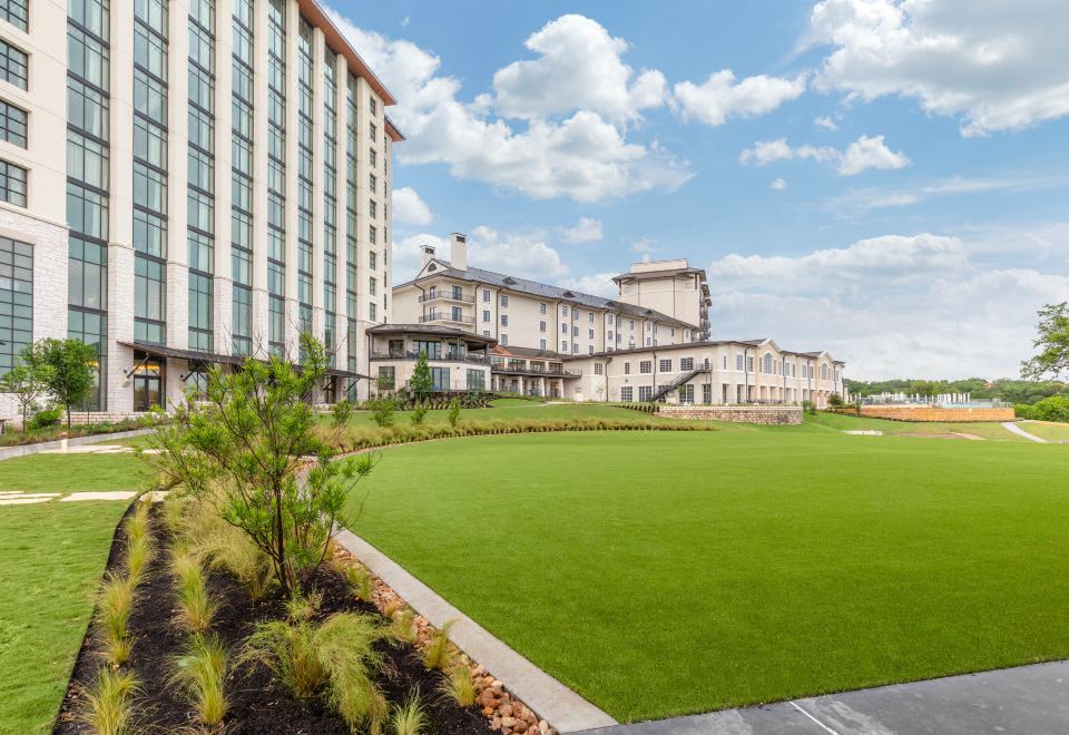 a large building with a green lawn in front of it , surrounded by trees and grass at Omni Barton Creek Resort and Spa Austin