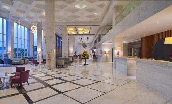 a large , modern hotel lobby with a marble floor , multiple couches , and potted plants , as well as a reception desk and a staircase at Radisson Hotel Agra