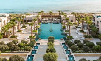 a luxurious beachfront resort with multiple pools , palm trees , and umbrellas , surrounded by clear blue water at Four Seasons Hotel Tunis