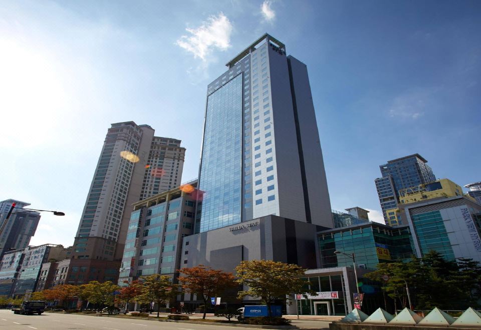 a tall building with a blue glass facade is surrounded by other buildings and trees at Shilla Stay Dongtan