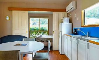 a kitchen with white cabinets , a dining table , and a small room with a refrigerator at Discovery Parks - Hobart